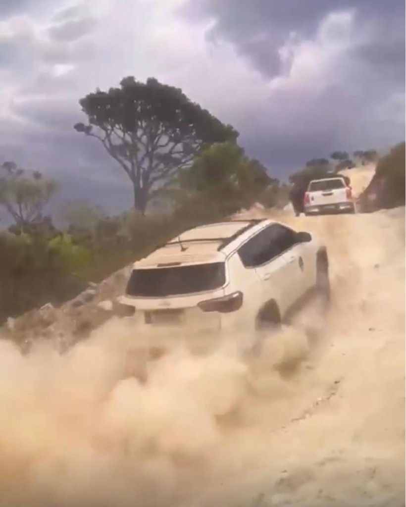 Veículo 4x4 subindo estrada de terra com poeira na serra
